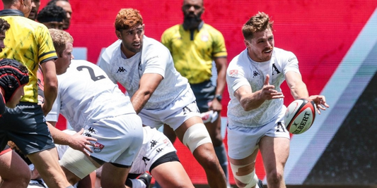 Major League Rugby action as an Anthem RC scrum-half passes the ball from the base of a ruck during their Round 2 match. Teammates in white jerseys provide support while a referee observes in the background.