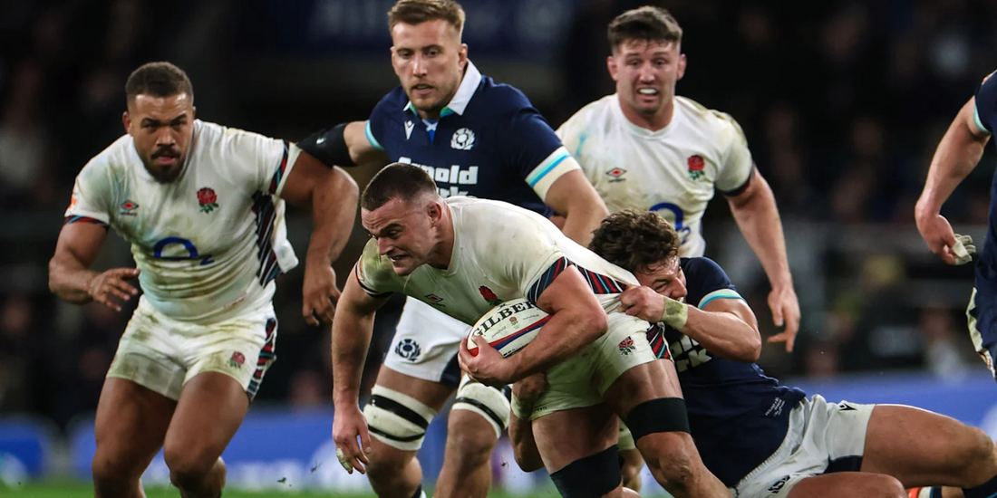 England and Scotland players in a physical battle during their Six Nations Round 3 clash at Twickenham. An England forward powers through a tackle as Scotland defenders attempt to bring him down, with teammates in pursuit.