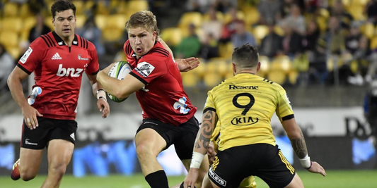 Super Rugby Pacific Round 1 action – Crusaders player running with the ball while being defended by a Hurricanes player during the 2025 season opener.