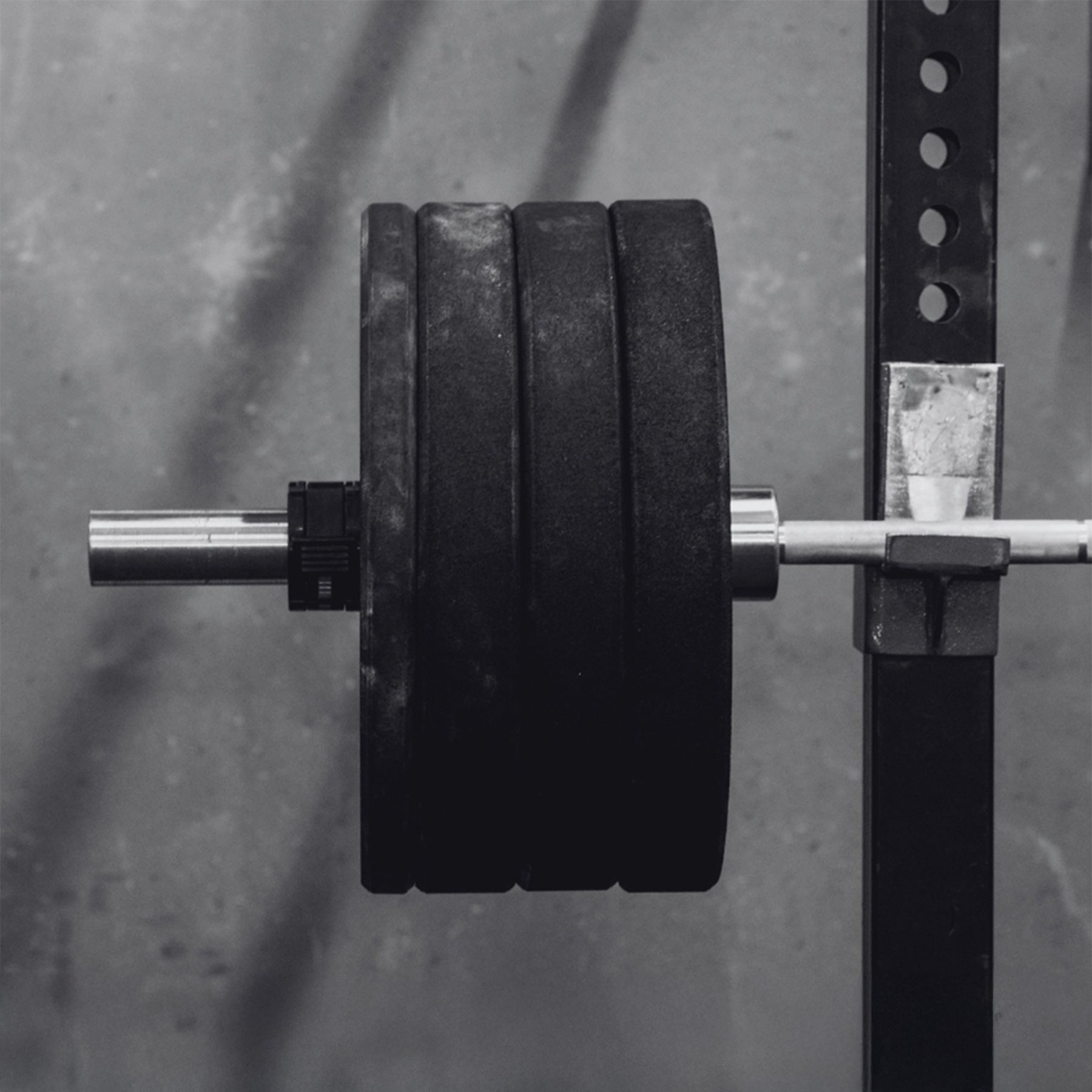 Black and white background image of a barbell with weight plates on a squat rack, set against a rugged gym wall. Optimized for mobile view as the hero banner image for the PEAK RUGBY Training Page.